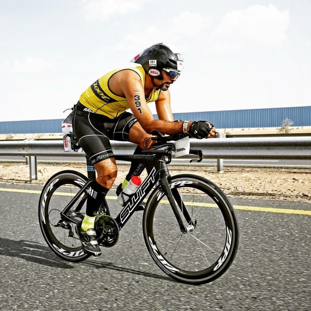 Nabil cycling in a triathlon, wearing a yellow race suit and aero helmet